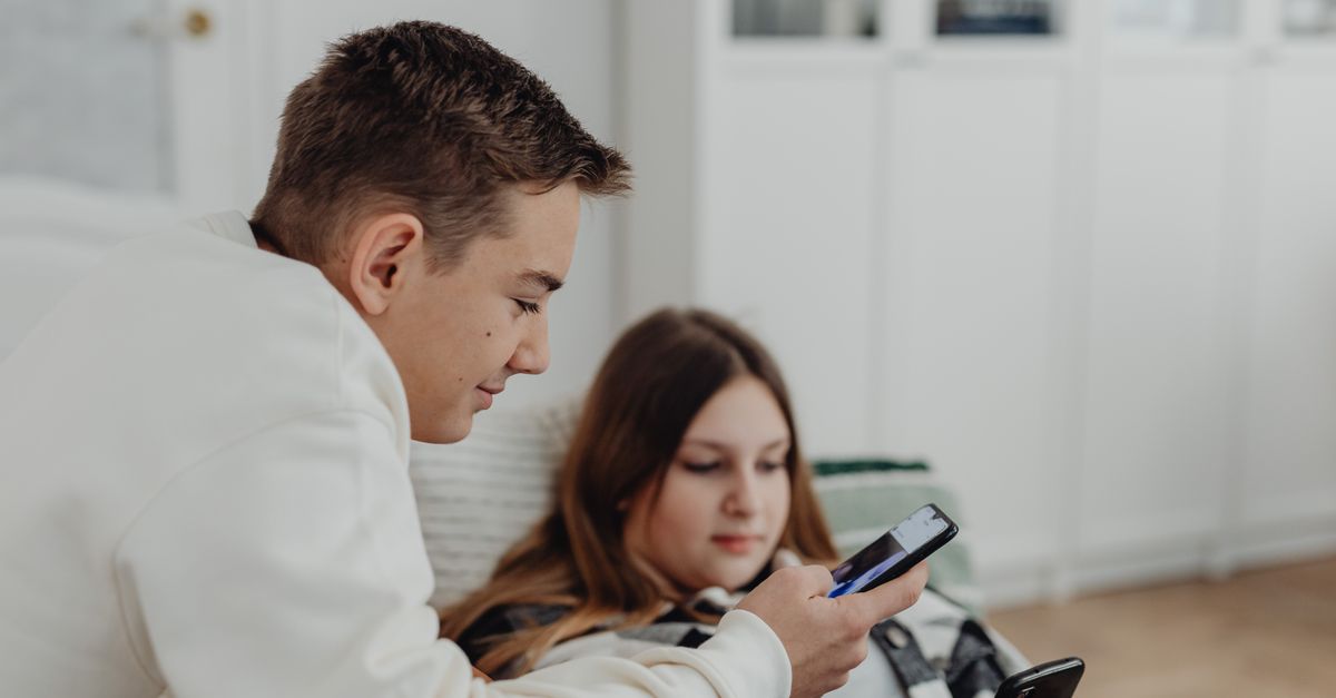 Two teenagers using smartphones in a cozy indoor setting, focused and relaxed.